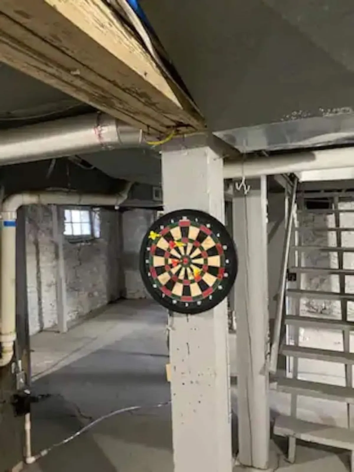 This image features a dartboard mounted on the wall, a visible staircase, and exposed pipes, creating a playful and informal setting ideal for friendly competitions and socializing with friends before or after heading out. The relaxed ambiance connects the group experience inside the home to the energetic nightlife and entertainment options nearby.