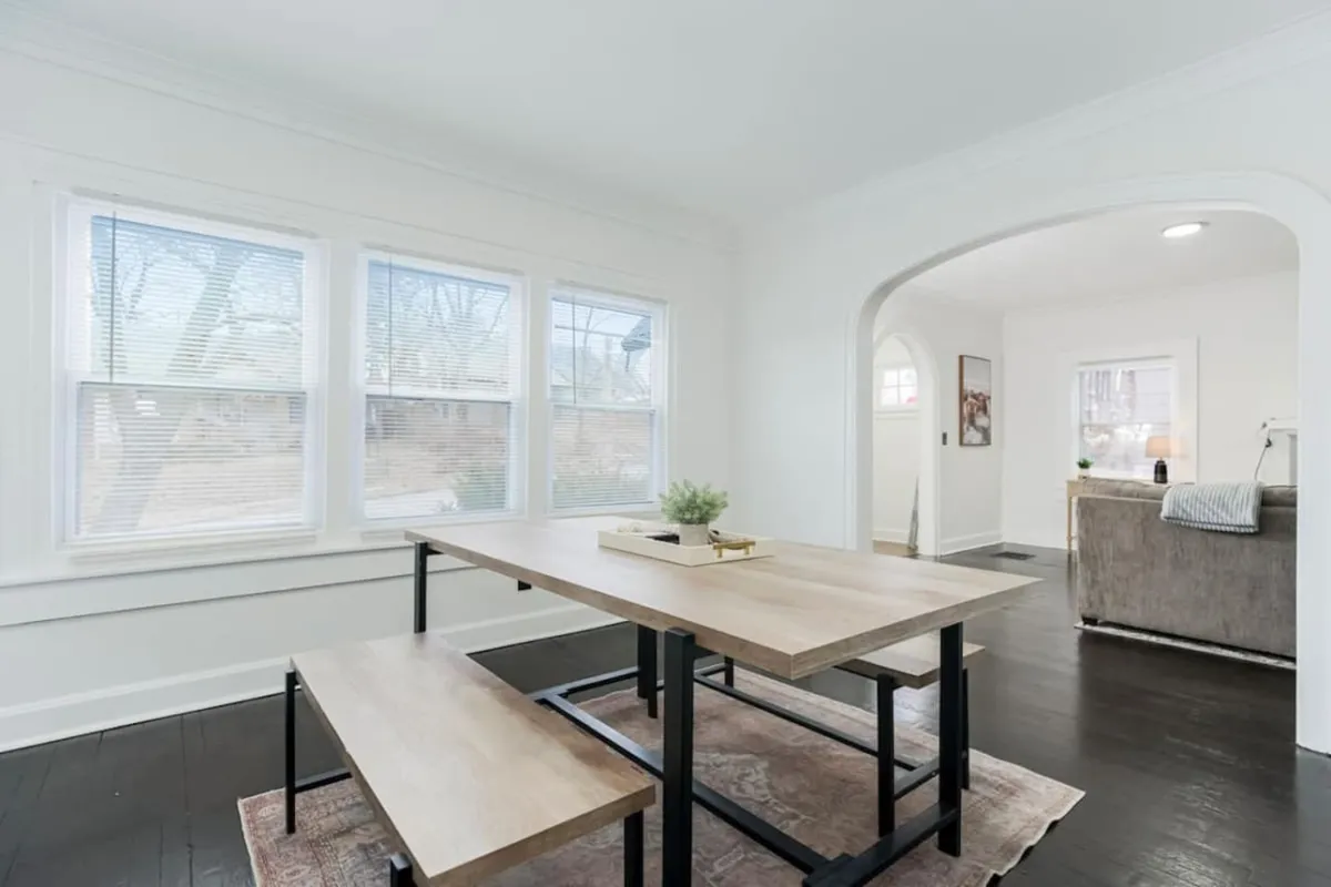 An inviting dining area sits bathed in natural light, with a large dining table perfect for group meals. The space seamlessly flows into the living room through a graceful archway, creating an open, welcoming environment ideal for family gatherings and shared moments.