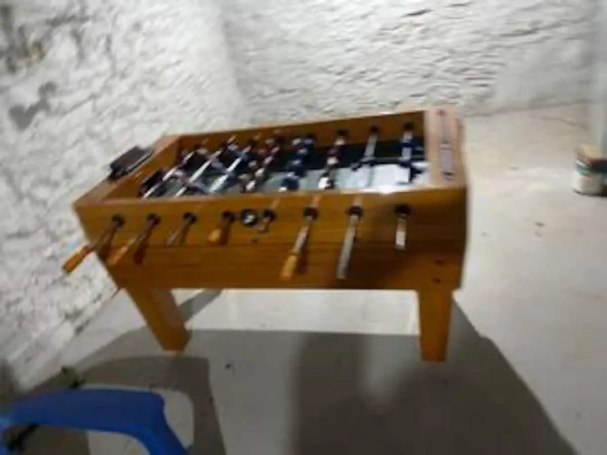 The image highlights a foosball table in a dimly lit basement space, with a blue chair nearby. The nostalgic and playful mood is perfect for casual gatherings and game nights, reflecting the energetic and communal aspect of group getaways.