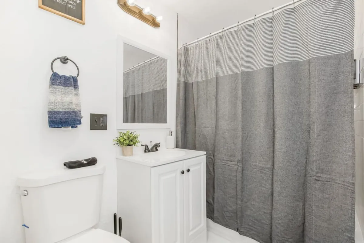 A bright, inviting bathroom is featured, complete with a sleek white vanity, mirror, shower curtain, and towel rack. The mood is serene and fresh, suggesting a space ideal for morning routines or relaxing self-care rituals.