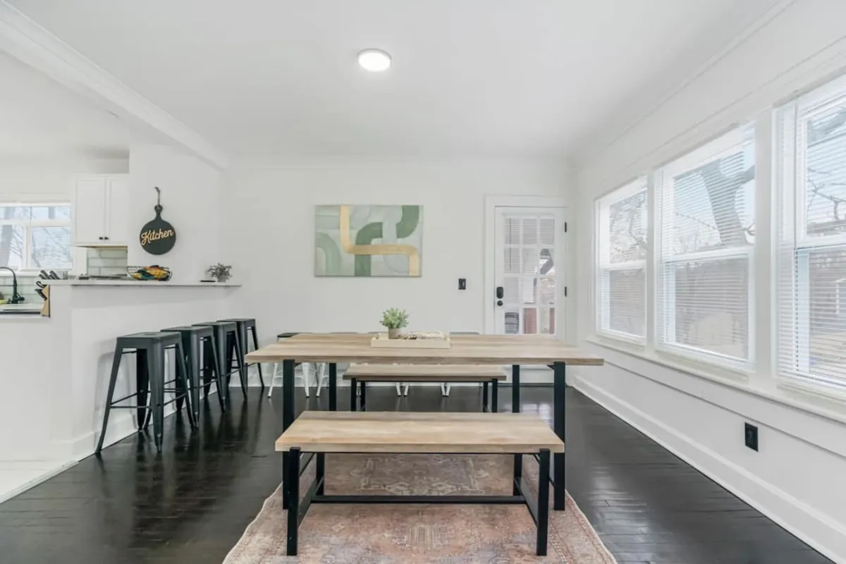 A welcoming dining area with a large table surrounded by chairs, bar stools along a countertop, modern artwork on the wall, and sunlight streaming through windows. This setup is ideal for group meals, celebrations, and casual socializing.
