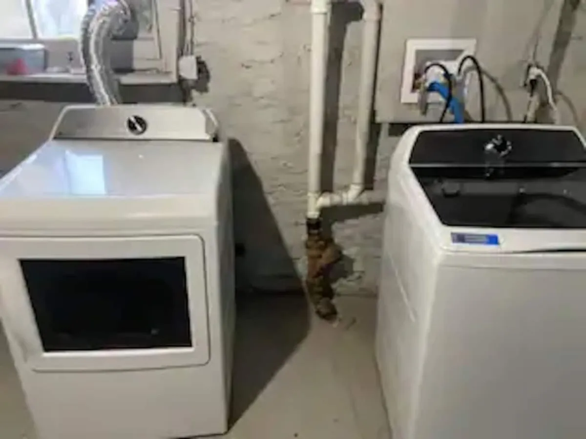 A bright, functional laundry room featuring a modern washing machine and dryer, with visible plumbing pipes and clean surfaces. The setup is clearly ready for guests to handle laundry duties with ease, emphasizing convenience and self-sufficiency.